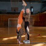 Two girls having fun practicing gymnastics in a sunny indoor sports hall.