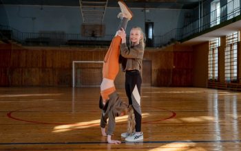 Two girls having fun practicing gymnastics in a sunny indoor sports hall.