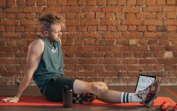 Athletic man sitting and resting on a mat in an urban gym, with a tablet and weights visible.